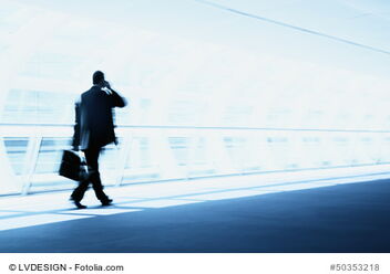 Manager mit Aktentasche und Handy am Ohr geht einen futuristisch anmutenden Weg entlang