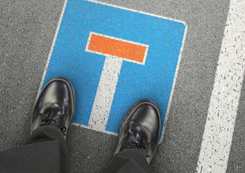 Zwei Schuhe stehen auf einem Sackgassen-Schild, das auf Asphalt gesprüht wurde