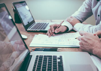 Ein Interim Manager bespricht mit einem Kollegen ein Projekt. Die Männer sitzen vor dem Laptop und haben Skizzen. Es sind nur die Hände zu sehen.